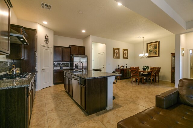 kitchen with dark brown cabinetry, stainless steel appliances, visible vents, dark stone counters, and tasteful backsplash