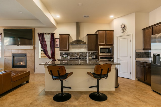 kitchen featuring visible vents, appliances with stainless steel finishes, dark stone counters, wall chimney exhaust hood, and a kitchen bar