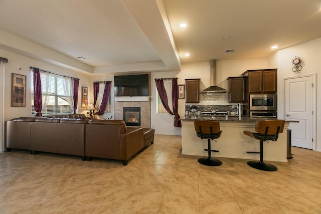 kitchen featuring a kitchen breakfast bar, open floor plan, wall chimney range hood, tasteful backsplash, and stainless steel microwave