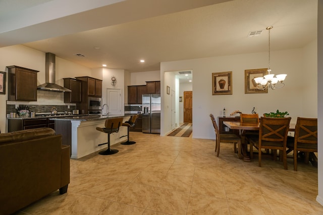 kitchen with appliances with stainless steel finishes, a sink, wall chimney range hood, dark brown cabinets, and a kitchen breakfast bar