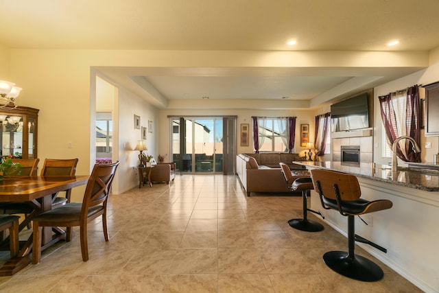 dining room with light tile patterned floors, a tray ceiling, baseboards, and a tiled fireplace