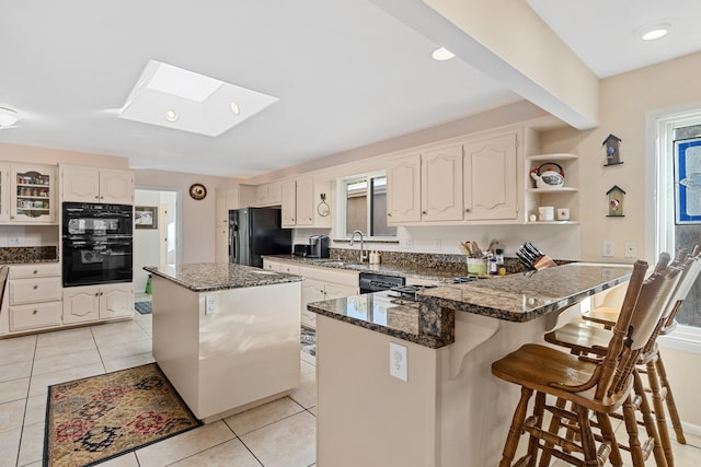 kitchen featuring a breakfast bar, a center island, a skylight, light tile patterned floors, and black appliances