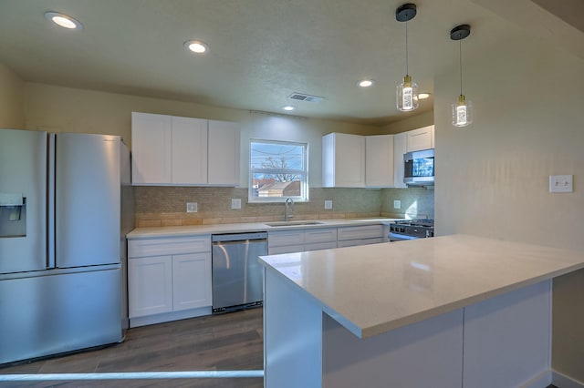 kitchen with appliances with stainless steel finishes, sink, white cabinets, decorative backsplash, and hanging light fixtures