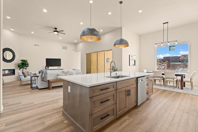 kitchen featuring pendant lighting, sink, dishwasher, an island with sink, and light wood-type flooring