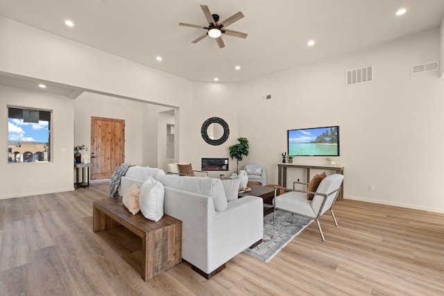 living room with a towering ceiling, light hardwood / wood-style floors, and ceiling fan