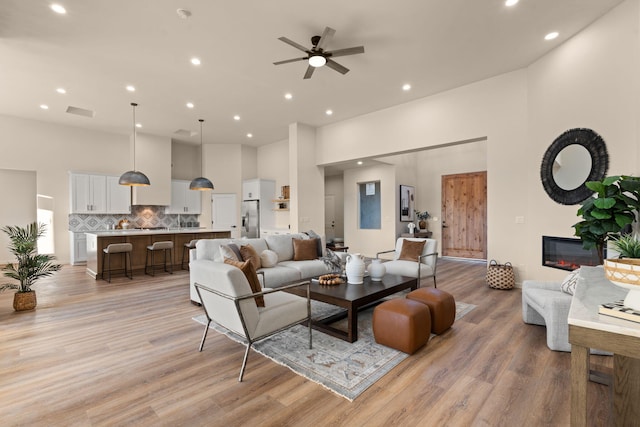 living room with light hardwood / wood-style floors, ceiling fan, and a high ceiling