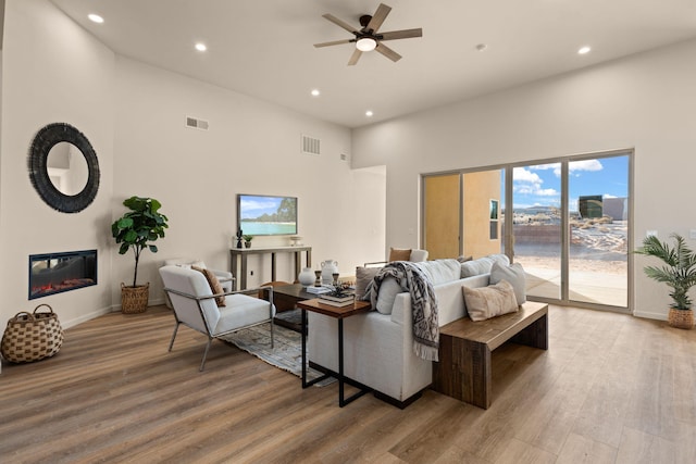 living room with ceiling fan, a towering ceiling, and light wood-type flooring