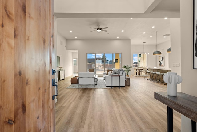 living room with ceiling fan, a towering ceiling, and light wood-type flooring