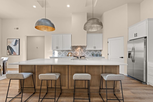 kitchen with white cabinetry, pendant lighting, a center island with sink, and stainless steel fridge