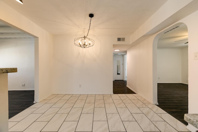 spare room with a textured ceiling, a chandelier, and light wood-type flooring