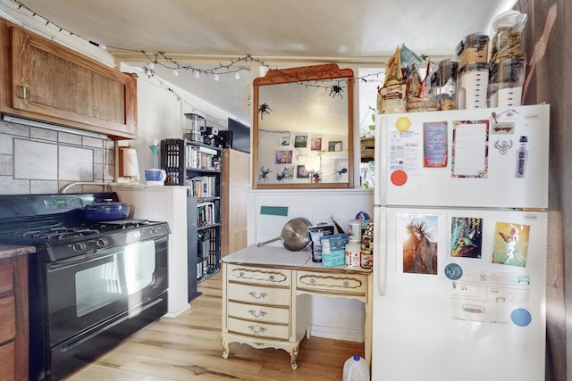 kitchen featuring white refrigerator, light hardwood / wood-style flooring, backsplash, and black gas range