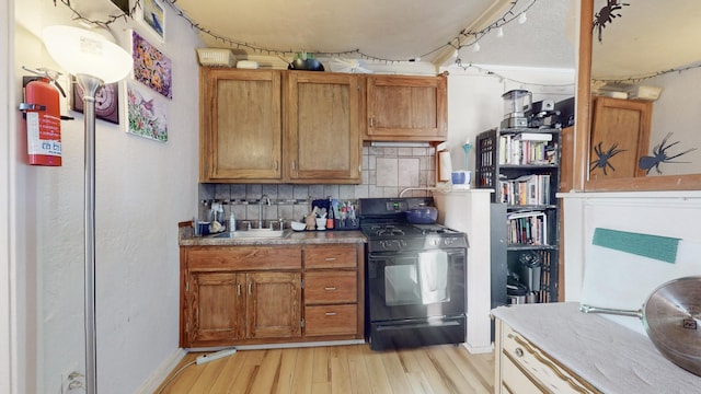 kitchen featuring tasteful backsplash, black range with gas cooktop, sink, and light wood-type flooring