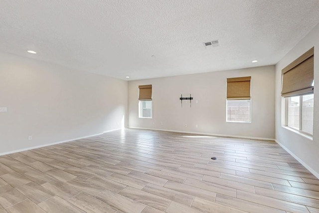 spare room with a textured ceiling, a healthy amount of sunlight, and light wood-type flooring