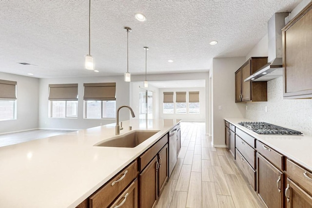 kitchen featuring appliances with stainless steel finishes, sink, decorative backsplash, hanging light fixtures, and wall chimney exhaust hood