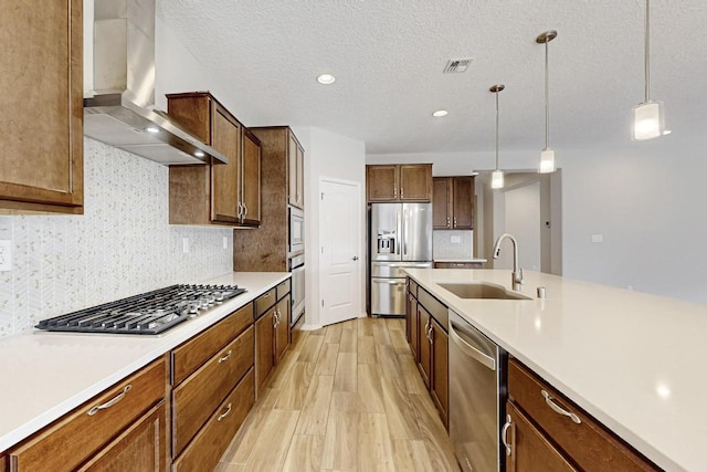 kitchen with pendant lighting, tasteful backsplash, sink, stainless steel appliances, and wall chimney range hood