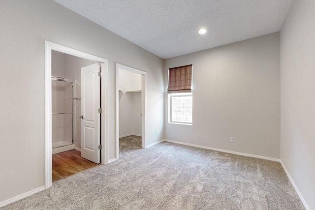 unfurnished bedroom featuring a walk in closet, light carpet, connected bathroom, and a textured ceiling