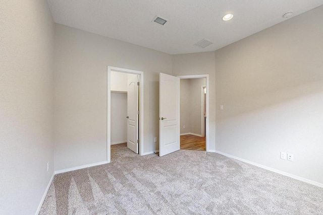 unfurnished bedroom featuring light carpet, a walk in closet, and a closet