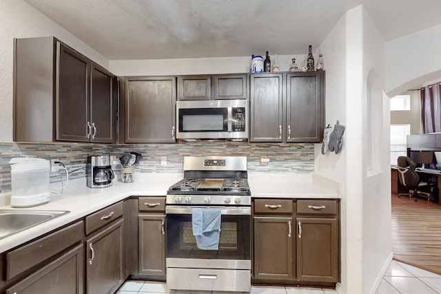 kitchen with light tile patterned floors, sink, backsplash, stainless steel appliances, and dark brown cabinetry