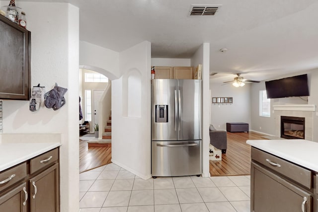 kitchen featuring a tile fireplace, light tile patterned floors, ceiling fan, and stainless steel fridge with ice dispenser