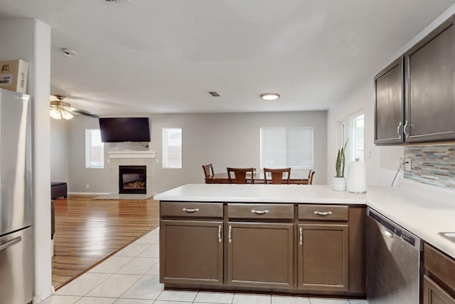 kitchen with appliances with stainless steel finishes, decorative backsplash, a tiled fireplace, light tile patterned floors, and kitchen peninsula