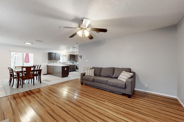 living room with ceiling fan, light hardwood / wood-style flooring, and a textured ceiling