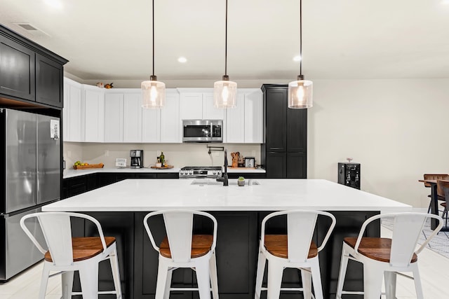 kitchen with sink, a breakfast bar, appliances with stainless steel finishes, hanging light fixtures, and a center island with sink