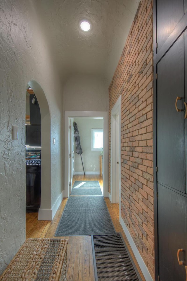 hallway featuring brick wall, a textured ceiling, and light hardwood / wood-style flooring