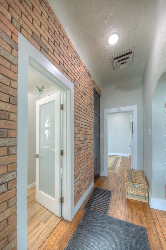 corridor featuring brick wall, light hardwood / wood-style flooring, and a textured ceiling