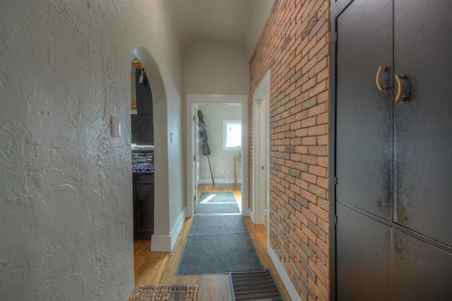 hallway featuring brick wall and light hardwood / wood-style flooring