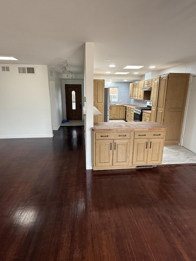 kitchen featuring dark wood-type flooring, appliances with stainless steel finishes, kitchen peninsula, wall chimney exhaust hood, and light brown cabinets