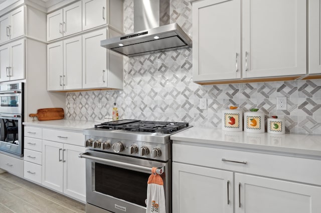 kitchen with appliances with stainless steel finishes, wall chimney range hood, light stone countertops, decorative backsplash, and white cabinets