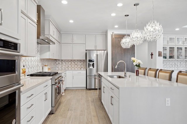 kitchen with high quality appliances, an island with sink, white cabinets, hanging light fixtures, and wall chimney exhaust hood