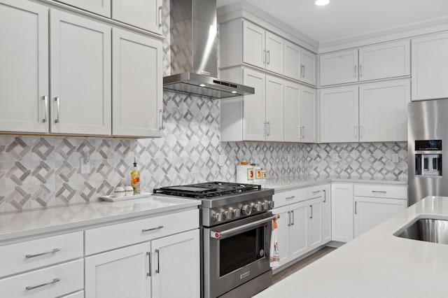 kitchen featuring white cabinetry, stainless steel appliances, backsplash, and wall chimney range hood