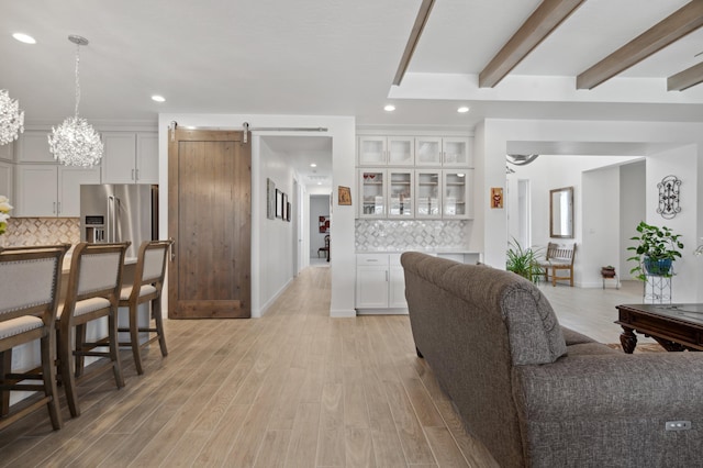 living room with a barn door, beam ceiling, and light wood-type flooring