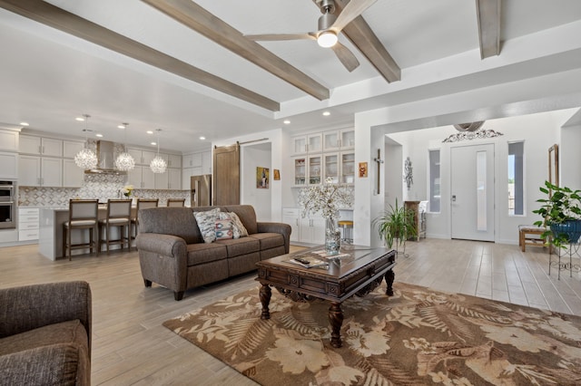 living room with a barn door, ceiling fan, beam ceiling, and light hardwood / wood-style floors