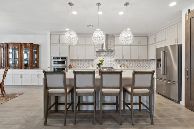 kitchen with a center island with sink, appliances with stainless steel finishes, a breakfast bar, and wall chimney range hood