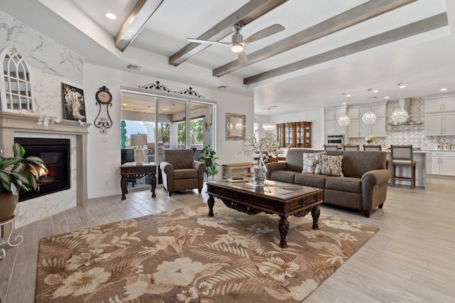 living room featuring beam ceiling, a premium fireplace, ceiling fan, and light wood-type flooring