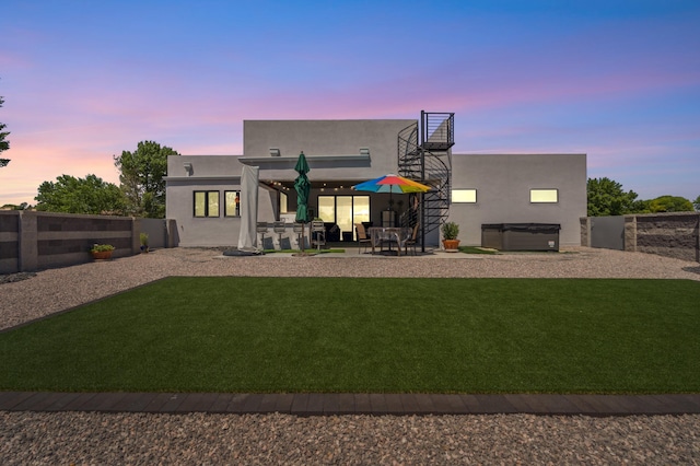 back house at dusk featuring a yard, a patio area, and a hot tub