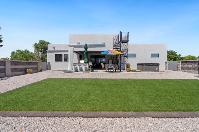 back of house with a hot tub, a patio, and a lawn