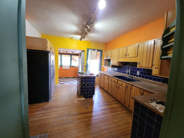 kitchen featuring stainless steel refrigerator, wood-type flooring, sink, decorative backsplash, and a center island