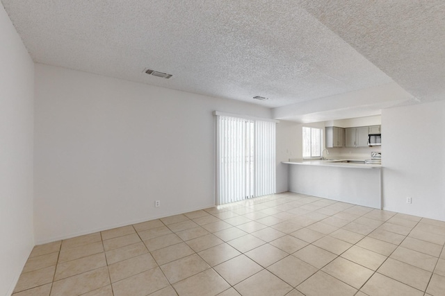 unfurnished living room featuring light tile patterned floors, sink, and a textured ceiling