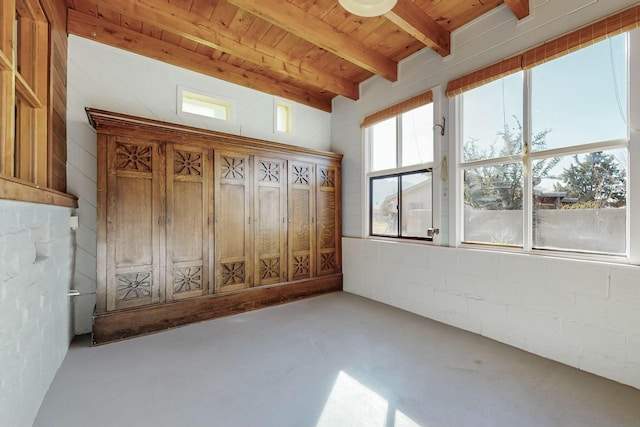 empty room with beam ceiling, concrete flooring, and wooden ceiling