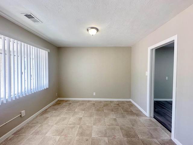 unfurnished room with a textured ceiling, visible vents, and baseboards