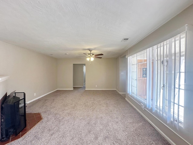 unfurnished living room with baseboards, visible vents, a wood stove, a textured ceiling, and carpet floors