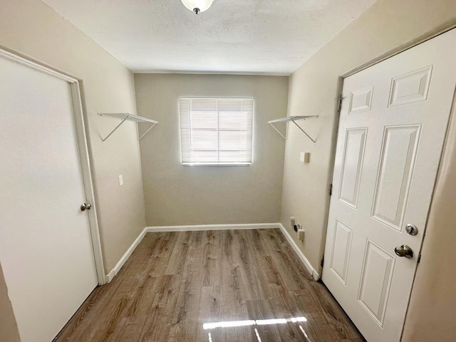 clothes washing area with laundry area, baseboards, light wood finished floors, and a textured ceiling