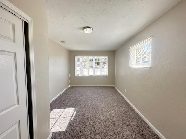 carpeted spare room with a textured ceiling, a textured wall, visible vents, and baseboards