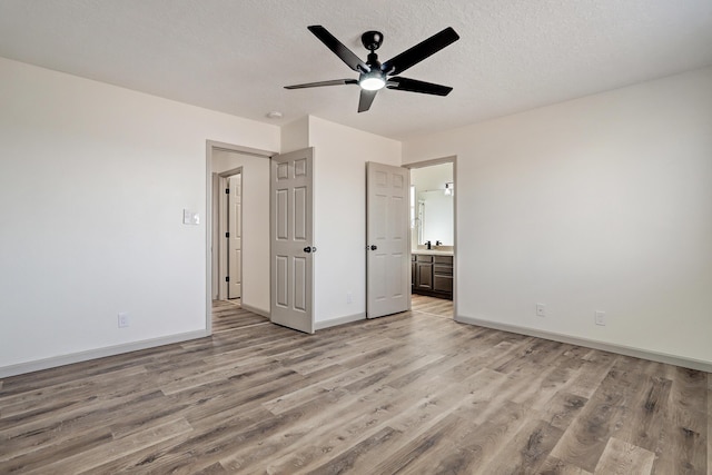 unfurnished bedroom with baseboards, connected bathroom, a textured ceiling, and light wood finished floors