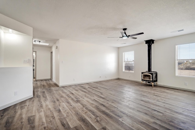 unfurnished living room featuring a textured ceiling, light wood-type flooring, a wood stove, and a ceiling fan