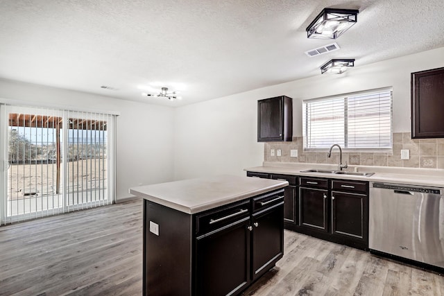 kitchen featuring visible vents, a kitchen island, light countertops, stainless steel dishwasher, and a sink