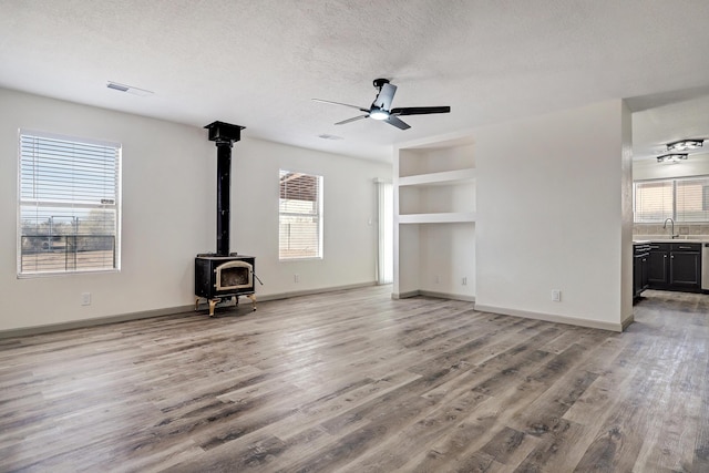 unfurnished living room featuring a ceiling fan, a wood stove, a textured ceiling, wood finished floors, and baseboards